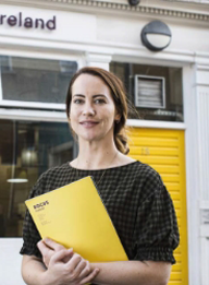 worker holding a yellow folder on her arms, with the focus ireland building on her background.