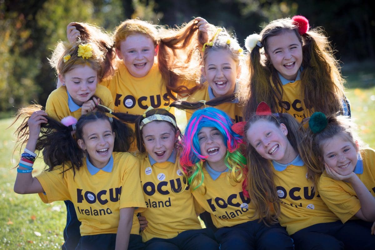 group of 9 young, female friends smiling at the camera. all of them are wearing hair accessories