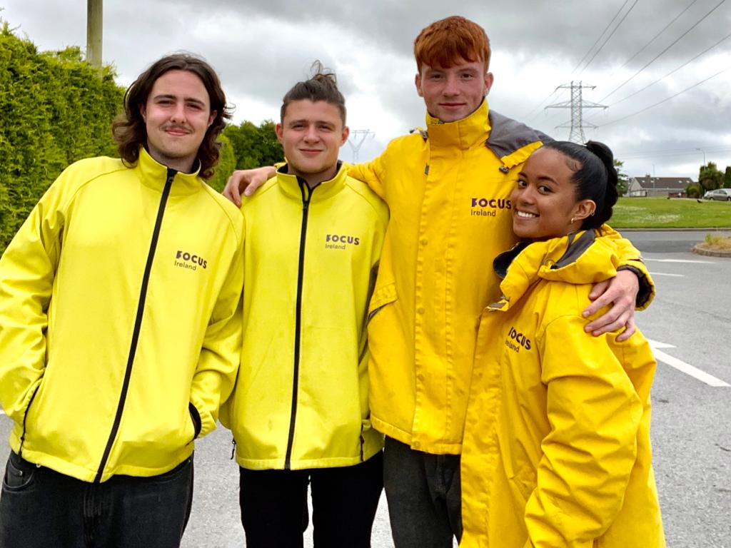 Members of the Cork door to door team stand together smiling. They are all wearing yellow Focus Ireland Jackets.