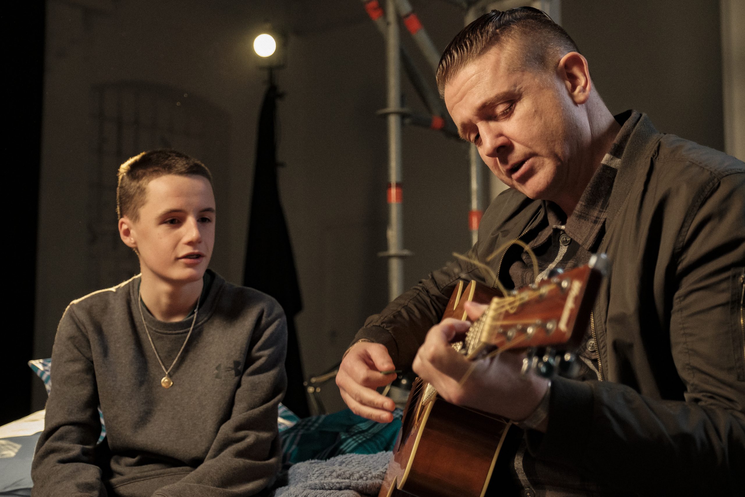 Damien Dempsey plays the guitar as a child looks on.