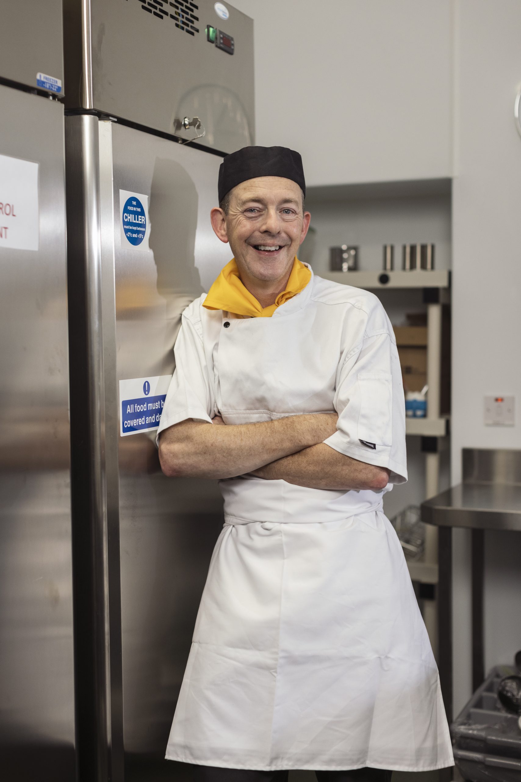 Focus Ireland Family Centre Kitchen staff smiling to the camera. He is leaning against a large stainless steel fridge with his arms crossed.