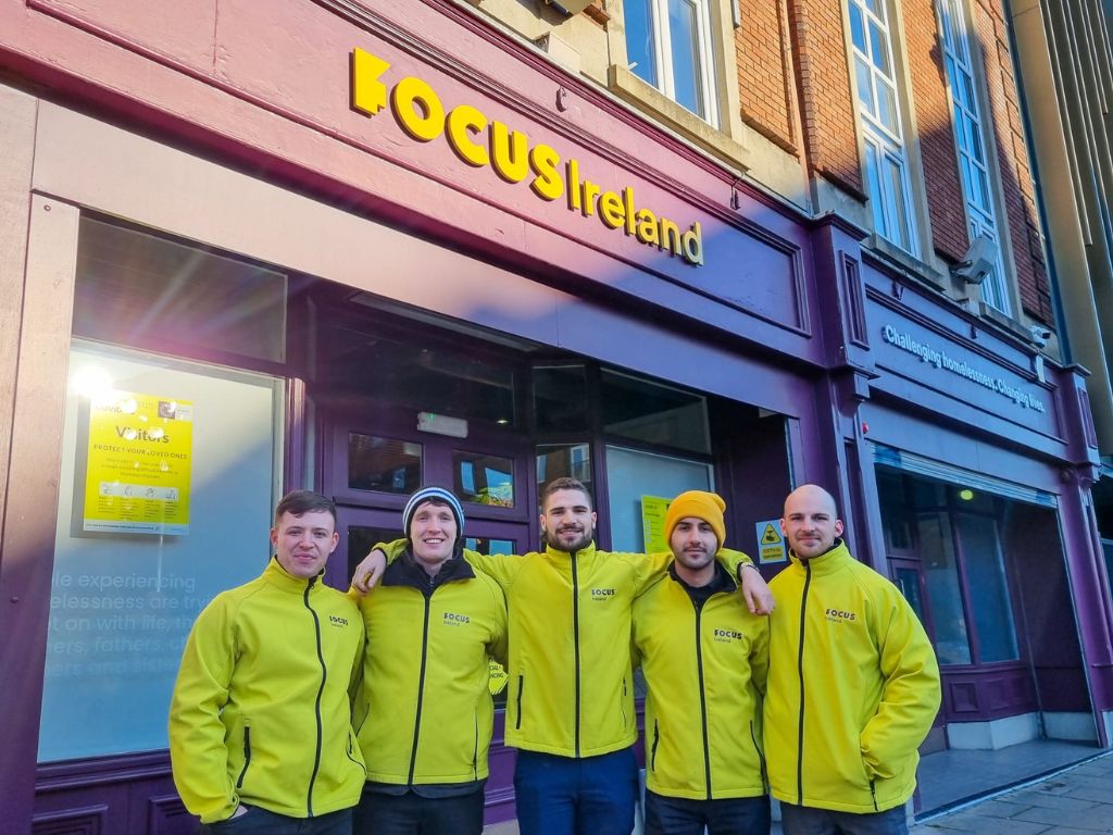 Members of the Focus Ireland door to door fundraising team stand together smiling. They are all wearing yellow Focus Ireland Jackets.