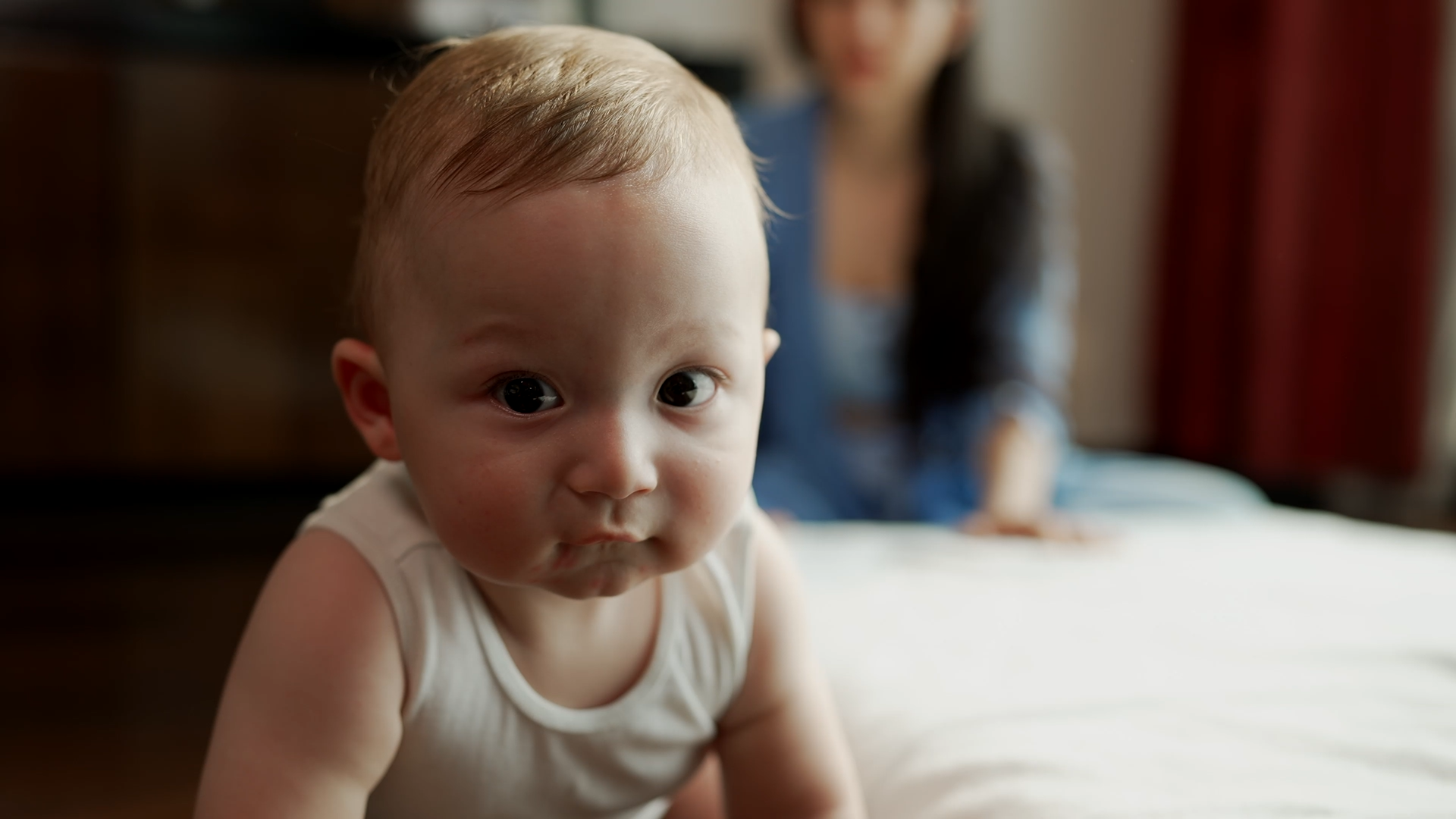 A baby crawls towards camera. We can see the outline of it's parent in the background.