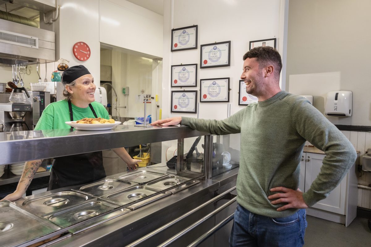 A chef at the Focus Ireland Coffee Shop chats with a customer. They are both smiling.