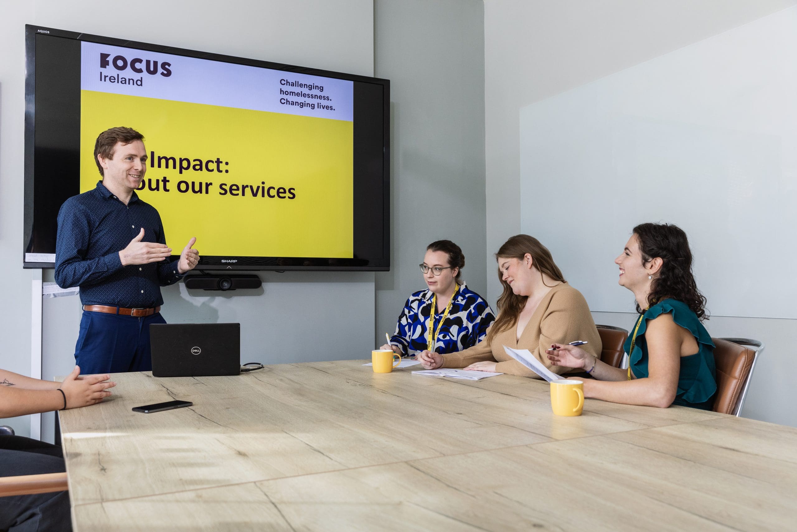 A Focus Ireland employee presents a powerpoint to their team. Four other members of staff are sitting at the table taking notes and smiling.