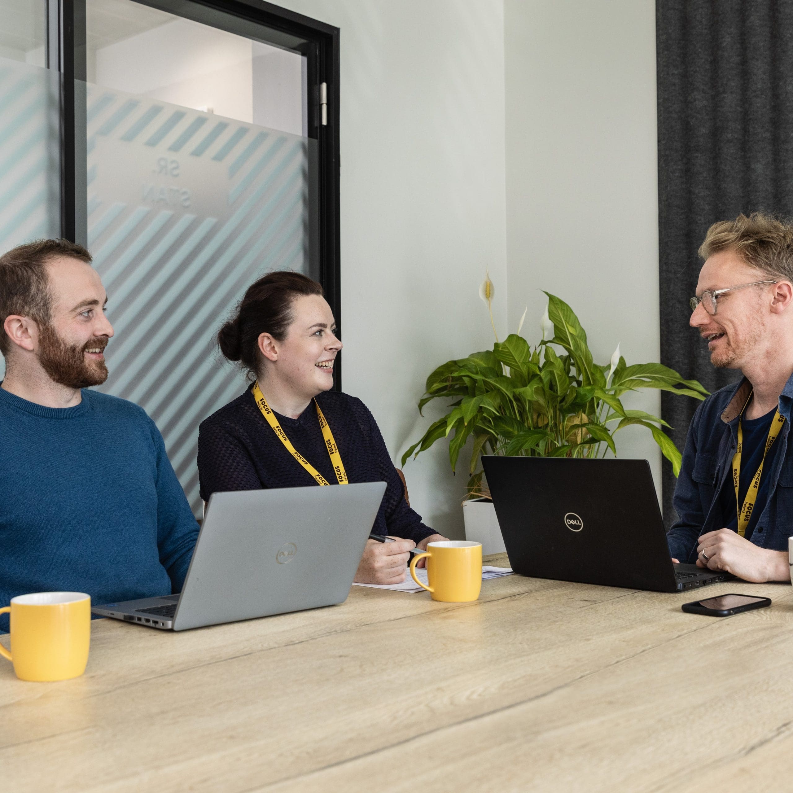 Three Focus Ireland employees sit at a meeting table. One member of staff is talking as the other two listen.