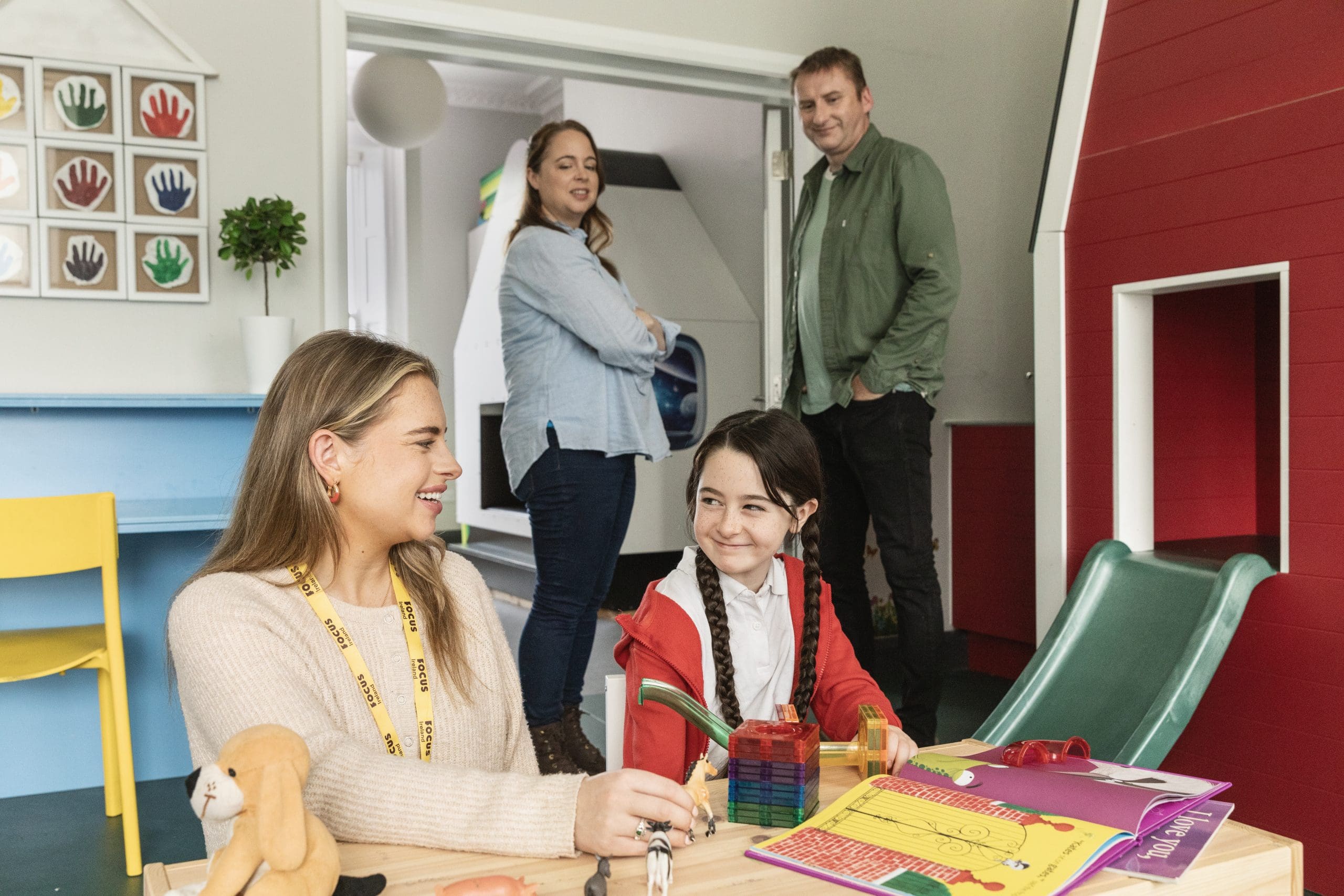 A Focus Ireland employee speaks to a child at the Family centre as the child's parents stand in the background smiling.