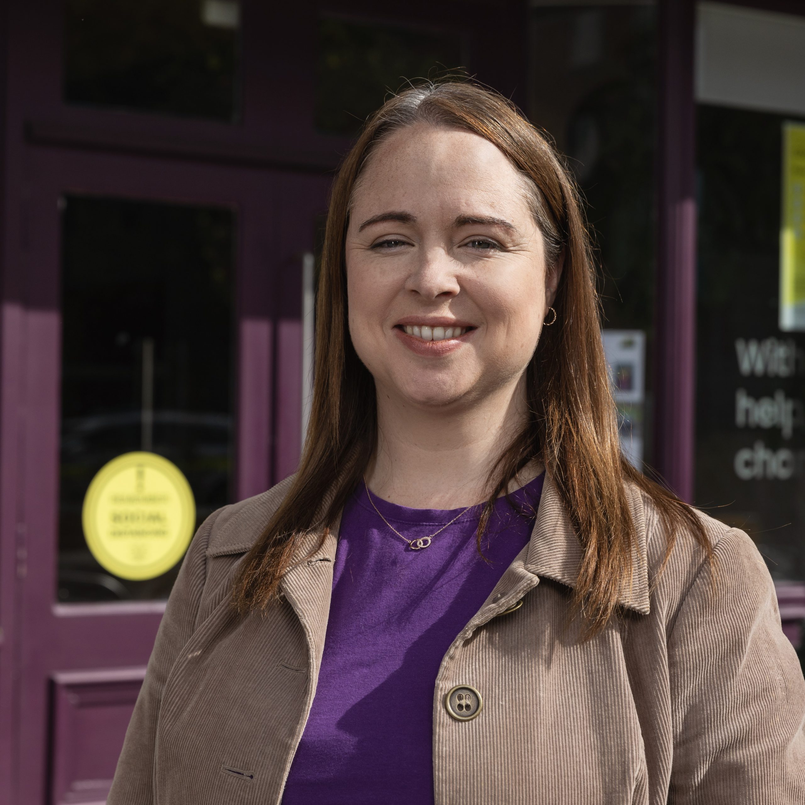 A Focus Ireland customer smiles to camera. She is wearing a brown corduroy jacket and a purple t shirt.