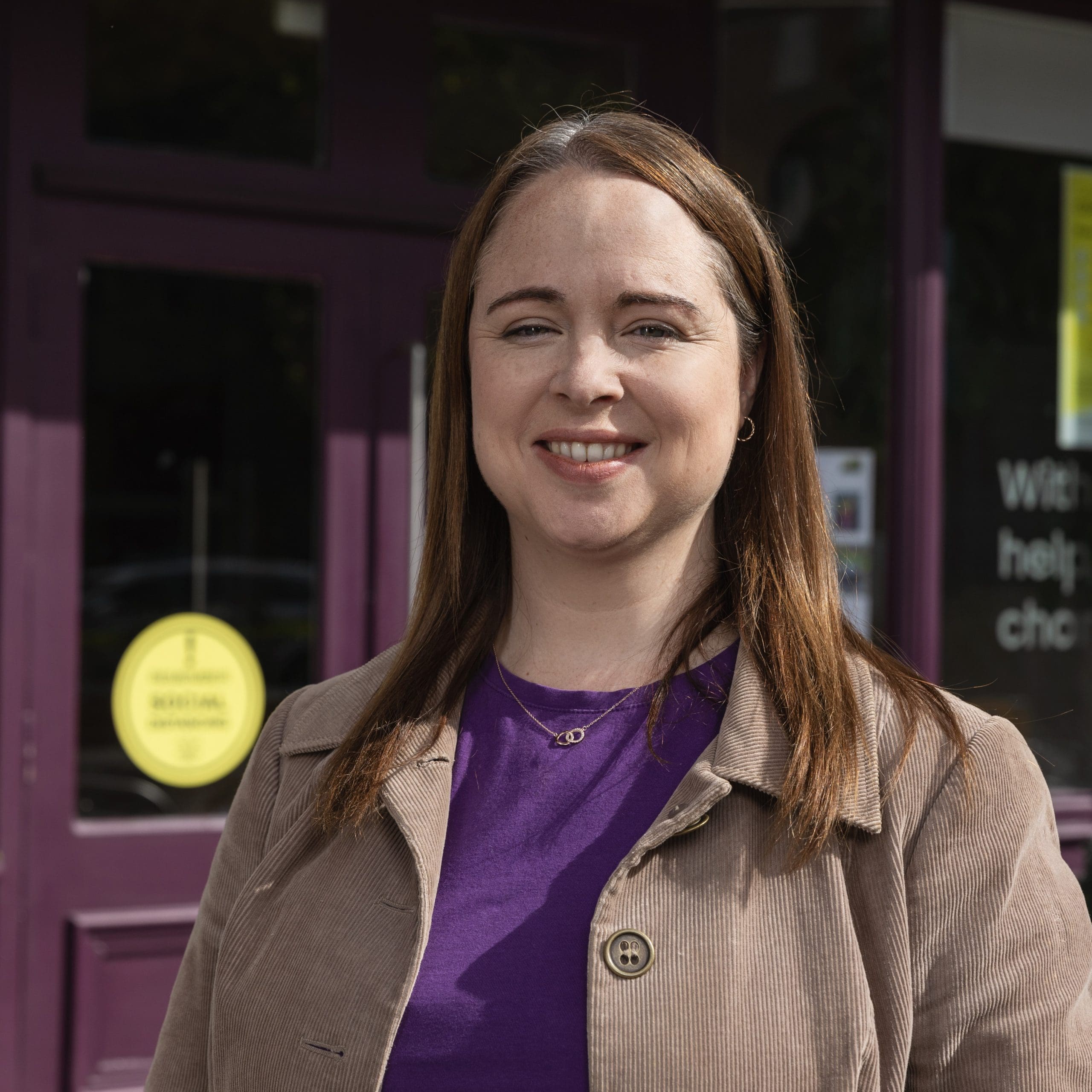 A Focus Ireland customer smiles to camera. She is wearing a brown corduroy jacket and a purple t shirt.