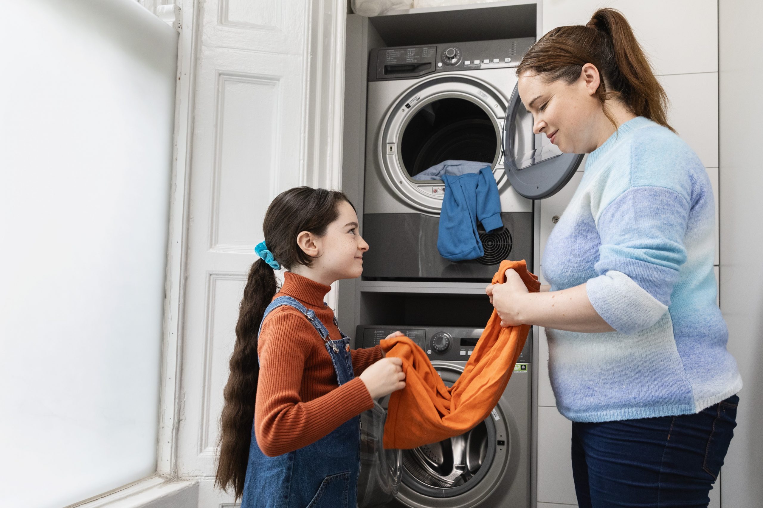 A mother and daughter help each other fold laundry.