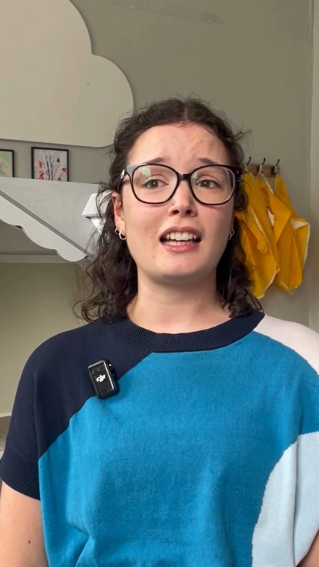 Dee Burke is speaking to camera. They have black hair and is wearing a blue jumper