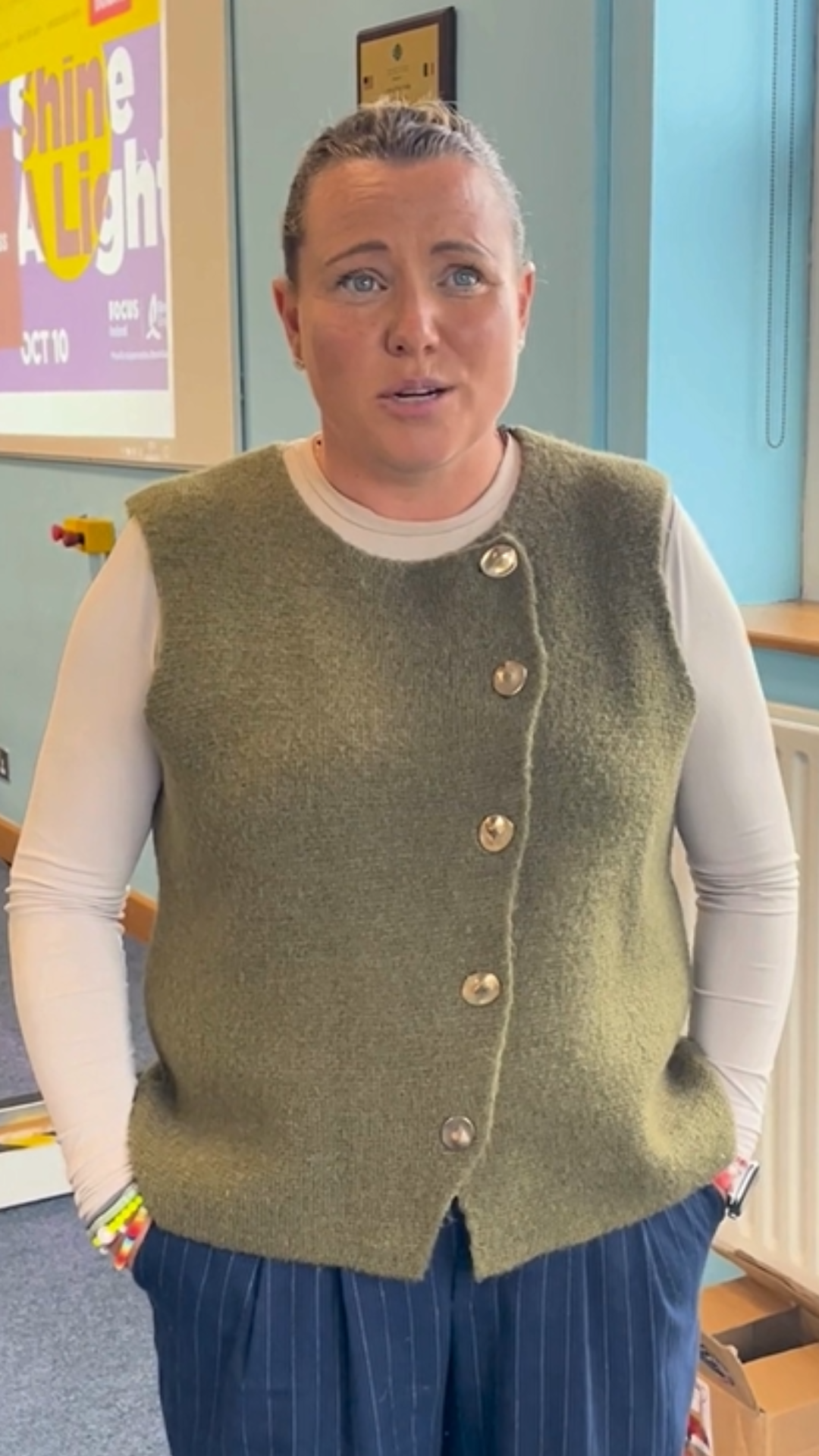 Jane Coyne speaks to camera. They have blonde hair and is wearing a green jumper