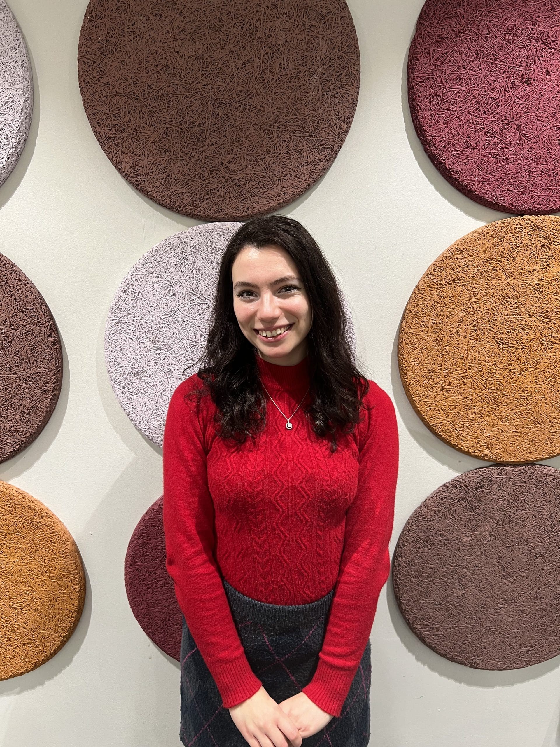 A photo of Assia Bouno. They is standing in front of a colourful wall